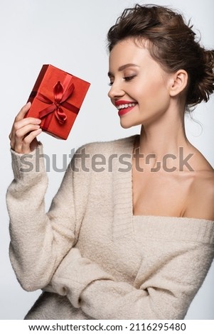 Happy model in cozy sweater holding red gift box isolated on white