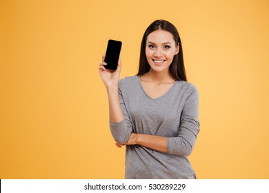 Happy model with phone in studio looking at camera. isolated orange background