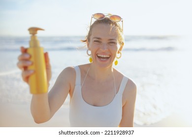 Happy Modern 40 Years Old Woman In White Swimwear At The Beach Using Sunscreen.