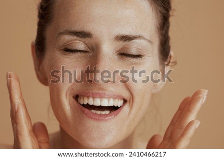 happy modern middle aged woman with wet face washing isolated on beige background.