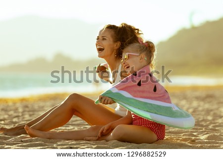 happy modern mother and child in swimwear on the seashore in the evening having fun time wrapped in watermelon towel. minimal to no crowd peace. Fun beach-friendly activities for the whole family.