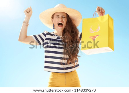 happy modern woman in straw hat against blue sky with yellow shopping bag with bikini rejoicing