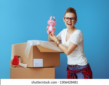 Happy Modern Woman In White T-shirt Near Cardboard Box With Old Toy Isolated On Blue