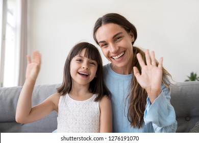 Happy Mom And Cute Kid Daughter Waving Hands Looking At Camera, Portrait Of Friendly Mother Or Baby Sitter And Child Girl Smiling Talking At Webcam Saying Hello Hi Or Goodbye Making Online Call Vlog