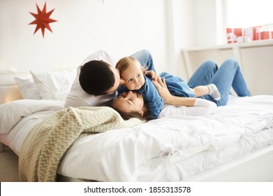 Happy Mom Dad And Daughter Playing On The Bed In The Bedroom On Christmas Morning.