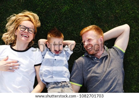 Happy mom, dad and their little son lie on green grass