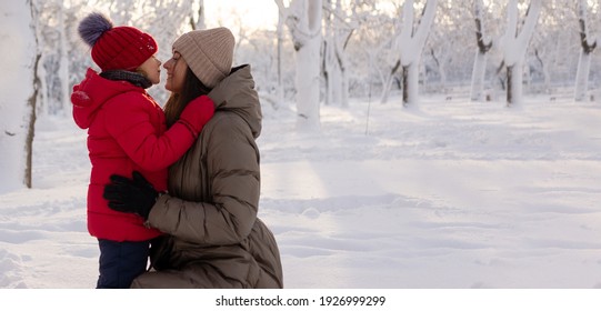 Happy Mom And Daughter 6 Years Old Hugging In A Winter Snowy Park. Family And Childhood Concept. Children's Entertainment In Winter. Place For Text.