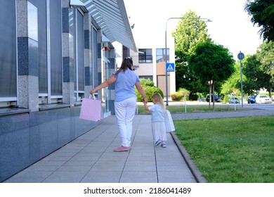 Happy Mom And Daughter Hold Shopping Bags Together, Defocused Woman And Child Of 3-4 Years Old Go Out Of Store, Girl In Fashionable Clothes, Shopping Concept, Happy Shopping On Black Friday