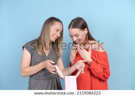 Happy mom and daughter are looking at fun shopping daughter is gesturing with her hands from happiness in red dress on blue background. Joyful moments of the relationship between derey and parents