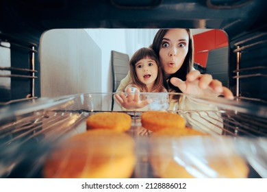 
Happy Mom And Daughter Reaching For Patties In The Oven. Cheerful Family Hungry By Dinner Tome Taking Out Meal From The Heated Stove
