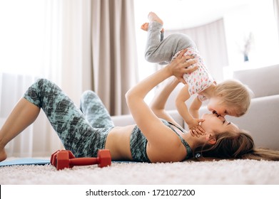 Happy Mom And Daughter. Young Mom With Her Little Cute Daughter. Mom Doing Sports At Home In A Sportswear And Has Fun With Her Baby On The Floor