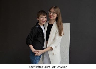 Happy Mom With Glasses And A Preschool-age Son, Hugging And Smiling On A Dark Background. A Family Of Two. Portrait Of Interesting People.