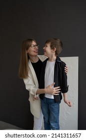 Happy Mom With Glasses And A Preschool-age Son, Hugging And Smiling On A Dark Background. A Family Of Two. Portrait Of Interesting People.