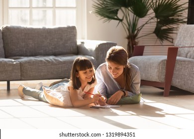 Happy Mom Helping Child Daughter Drawing With Colored Pencils Laying On Warm Floor Together, Smiling Baby Sitter Mother Teaching Cute Kid Learning Creative Activity Play Laugh At Home In Living Room