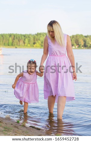 Happy mom and her little daughter in the same pink dresses play