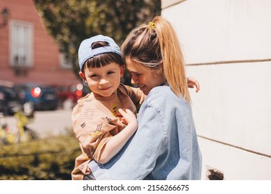 Happy Mom Holding Son Boy In Arms, Hugging Kid With Noses Touch, Smiling, Enjoying Warm Moment. Younger Mum Carrying Kid And Dancing On The Street. Motherhood, Adoption, Family Concept.