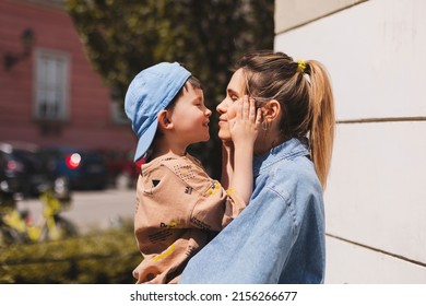 Happy Mom Holding Son Boy In Arms, Hugging Kid With Noses Touch, Smiling, Enjoying Warm Moment. Younger Mum Carrying Kid And Dancing On The Street. Motherhood, Adoption, Family Concept.