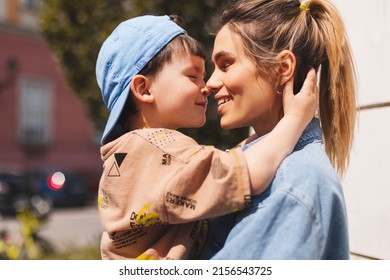 Happy Mom Holding Son Boy In Arms, Hugging Kid With Noses Touch, Smiling, Enjoying Warm Moment. Younger Mum Carrying Kid And Dancing On The Street. Motherhood, Adoption, Family Concept.