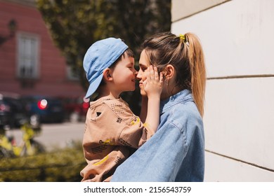 Happy Mom Holding Son Boy In Arms, Hugging Kid With Noses Touch, Smiling, Enjoying Warm Moment. Younger Mum Carrying Kid And Dancing On The Street. Motherhood, Adoption, Family Concept.