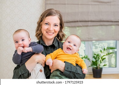 Happy Mom Holding Two Babies Twins At Home In The Bedroom, Smiling