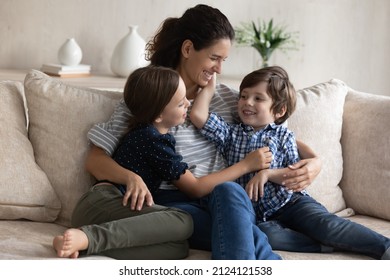 Happy Mom Hugging Little Son And Daughter With Love, Care, Tenderness, Relaxing With Kids In Couch, Talking To Children, Laughing. Mother And Two Siblings Enjoying Leisure At Home. Motherhood Concept