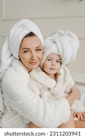 Happy mom hugs kid. Cheerful girls having beauty day at home. Young mother with cute little daughter in bathrobe, towels on heads sitting lovely on bed. Healthcare and family concept.  Closeup. - Shutterstock ID 2311203941