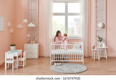 Happy Mom Is Interesting In Her Baby, In The Room, White Furniture Decor. Cradle And Crib Style.