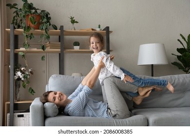 Happy mom lifting little daughter kid up in air, playing airplane with girl, lying on couch, keeping balance, doing acroyoga base with child, enjoying motherhood, active games, exercising - Shutterstock ID 2086008385
