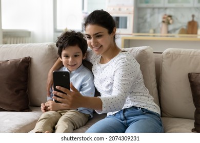 Happy Mom And Little Son Taking Home Selfie Together, Relaxing, Hugging On Sofa, Holding Mobile Phone, Looking At Screen, Smiling. Mother And Kid Making Video Call, Chatting Online