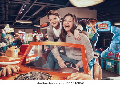 Happy Mom And Son Sitting On Toy Car. Spending Holiday Together With Family. Entertainment Center, Mall, Amusement Park. Family Rest, Leisure.