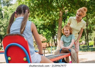 happy mom standing near children riding seesaw on playground - Powered by Shutterstock