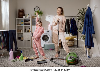 Happy Mom Teaching Little Girl To Clean Floor With Vacuum Cleaner In Laundry Room, Bathroom. Woman And Child Are Standing In The Middle Of The Room Fooling Around With Brush While Vacuuming.