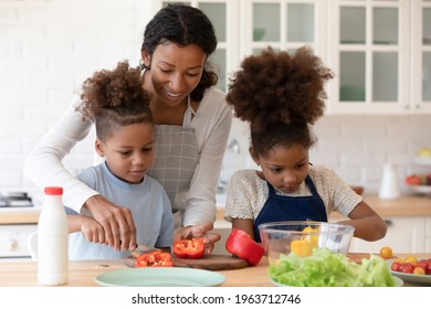 Happy mom teaching two preschooler kids to make vegetarian meal, slicing fresh pepper for salad. Mother and children cooking vegetables together in modern kitchen, keeping healthy eating diet - Powered by Shutterstock