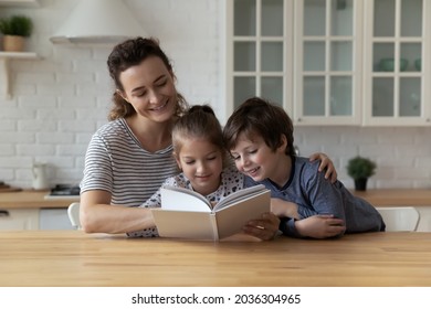 Happy Mom And Two Children Enjoying Book Story In Kitchen. Mother Entertaining Kids At Home, Teaching Boy And Girl To Read, Improving Imagination, Interest To Literature. Family Smart Activity