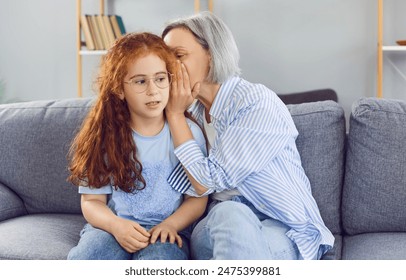 Happy moment in the family as a grandmother whispers a secret or gossip to her granddaughter. They are together, sharing a private talk filled with joy and hearsay, strengthening their bond. - Powered by Shutterstock