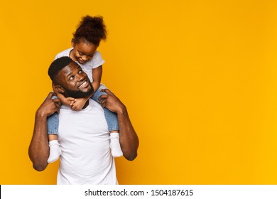 Happy moments. Cute african girl sitting on daddy's shoulders, orange background, empty space