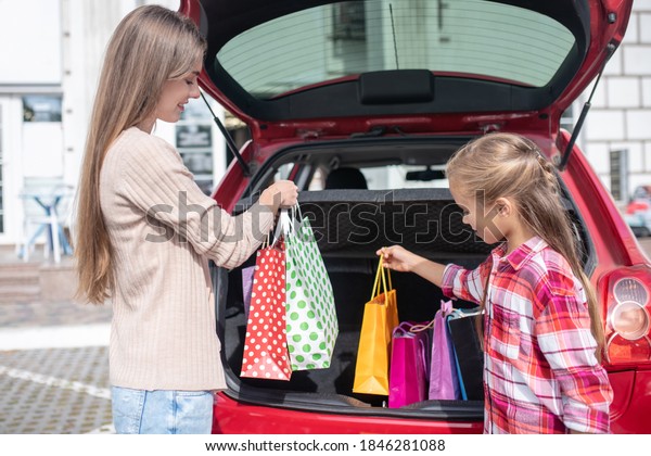 Happy moments. Mom and daughter taking out shopping\
bags from car boot