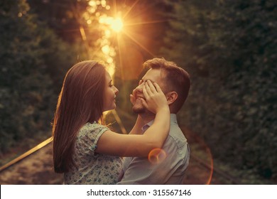 Happy Moments Of Young Couple At Summer Park Alley In Evening Sunlight. Girl Closing Boy's Eyes