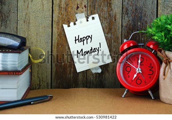 HAPPY MONDAY! text written on sticky note.\
Books, pen, spectacle and red clock on brown desk. Education and\
business concept.