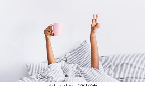 Happy morning. Hands of african american woman in blanket holds coffee, shows peace sign, panorama, free space - Powered by Shutterstock