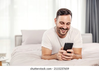 A happy morning man lying on the bed and flirting on the phone at his cozy apartment.