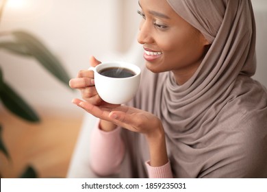 Happy morning. Happy Muslim woman in traditional hijab drinking strong black coffee at home. Smiling young lady having hot aromatic beverage, relaxing during her break
