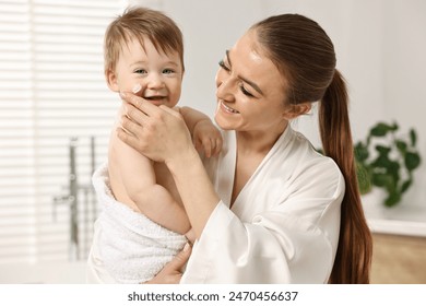 Happy mother applying moisturizing cream onto baby`s face in bathroom - Powered by Shutterstock