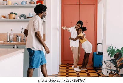 Happy mother arriving home to a warm welcome from her daughter and husband after travelling. Woman hugging her family at the doorway, excited to reunite with them after spending some time apart. - Powered by Shutterstock