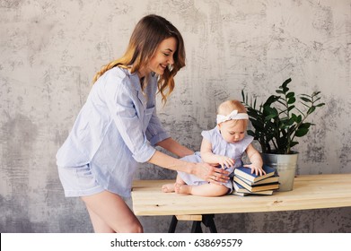 Happy Mother And Baby Daughter Playing At Home In Bedroom In Blue Matching Pajamas. Cozy Family Lifestyle In Modern Scandinavian Interior. 