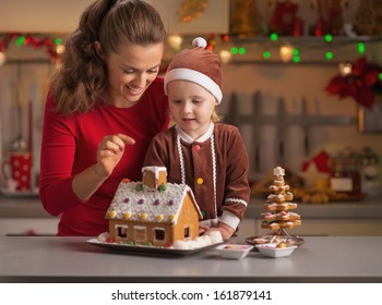 Happy Mother And Baby Decorating Christmas Cookie House In Kitchen