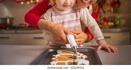 Happy mother and baby decorating homemade christmas cookies with glaze