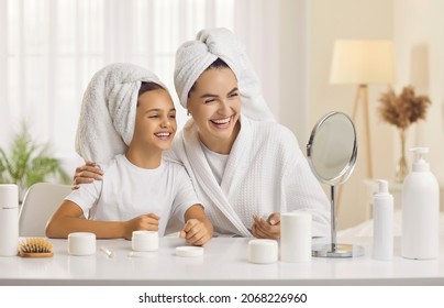 Happy mother and child enjoying morning skin care routine together. Cheerful beautiful mommy and little daughter looking in small mirror on beauty table in bedroom, applying face cream and laughing - Powered by Shutterstock