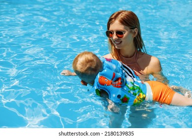 Happy Mother And Child In The Outdoor Swimming Pool Of A Tropical Resort. The Kid Is Learning To Swim. Mom And Child Play In The Water. Family Summer Vacation In An Exotic Place. Active