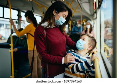 Happy Mother Communicating With Her Son While Commuting By Public Transport And Wearing Face Masks Due To COVID-19 Pandemic. 